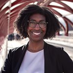 Sarah, a Black woman with dark curly hair and glasses, poses on the red Peace Bridge in Calgary