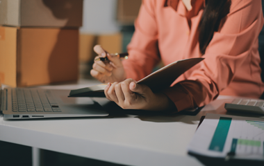 Person reviewing notes at a desk with a laptop, pen, and financial documents nearby.