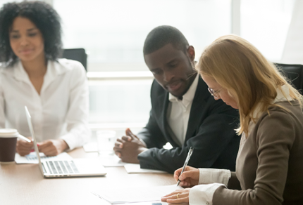 Three professionals collaborating at a meeting table while reviewing documents.