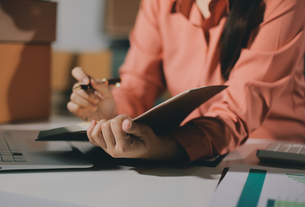 Person in professional attire writing on documents at a desk with a glass of water and a brass lamp in a courtroom or office setting.