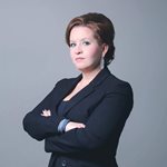 Kathy Briere, a woman with short brown hair, poses with her arms crossed wearing a dark suit