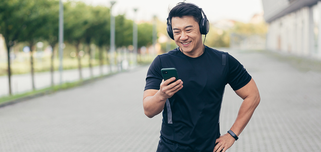 An Asian male on a morning run in the park listens to music and podcast on his phone.