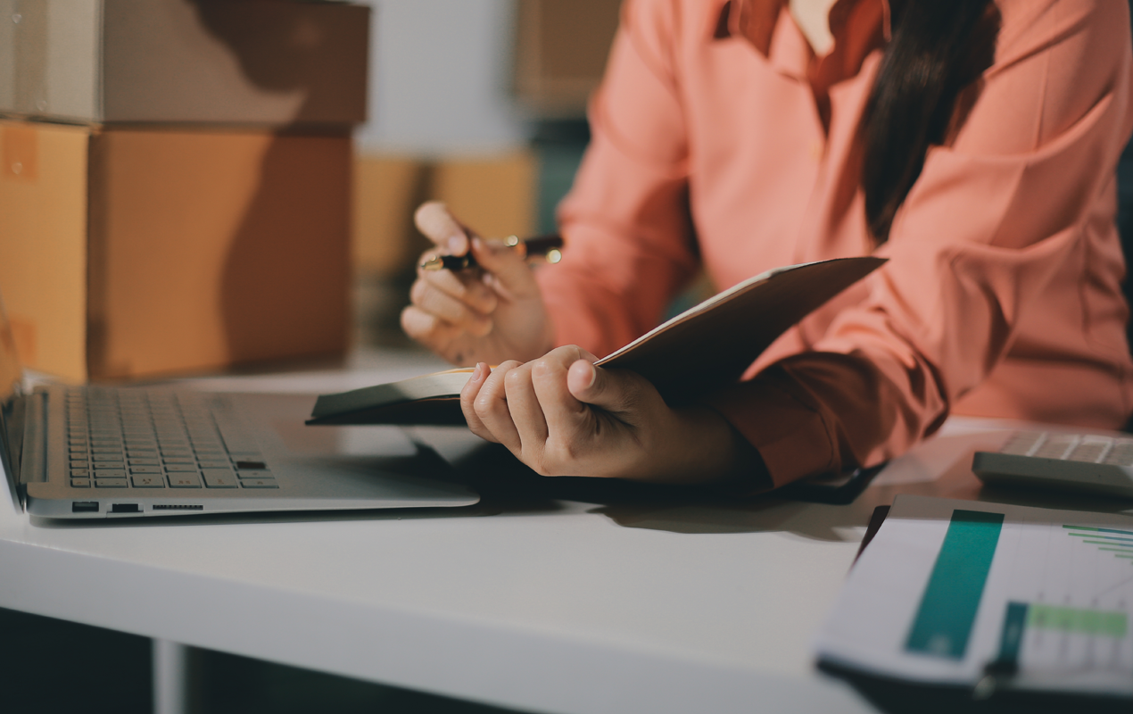 Person reviewing notes at a desk with a laptop, pen, and financial documents nearby.
